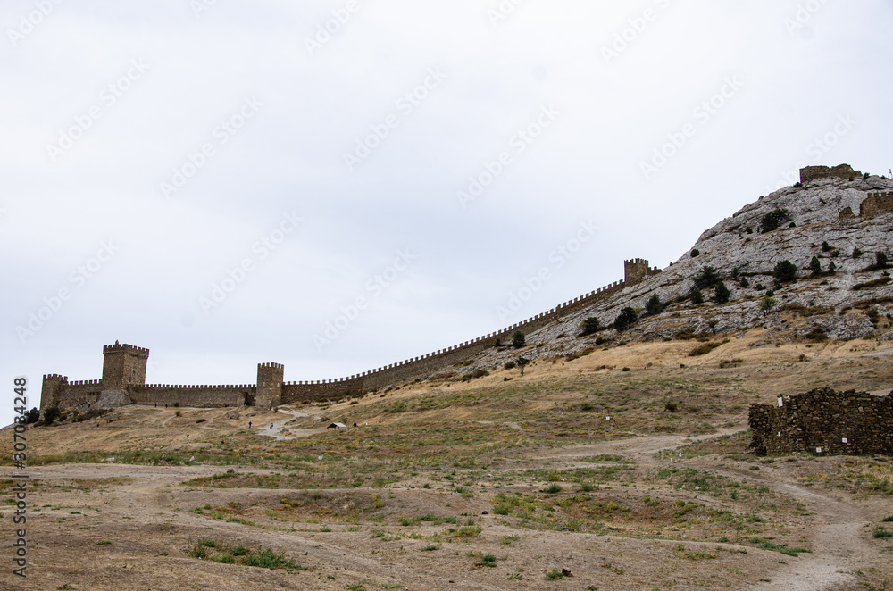 Old fortress in the mountains, a wall and towers on a cliff.