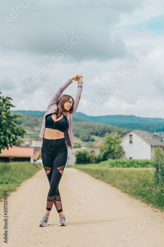 Outdoor portrait of young beautiful fit woman wearing black activewear, athlete model stretching, sport fashion