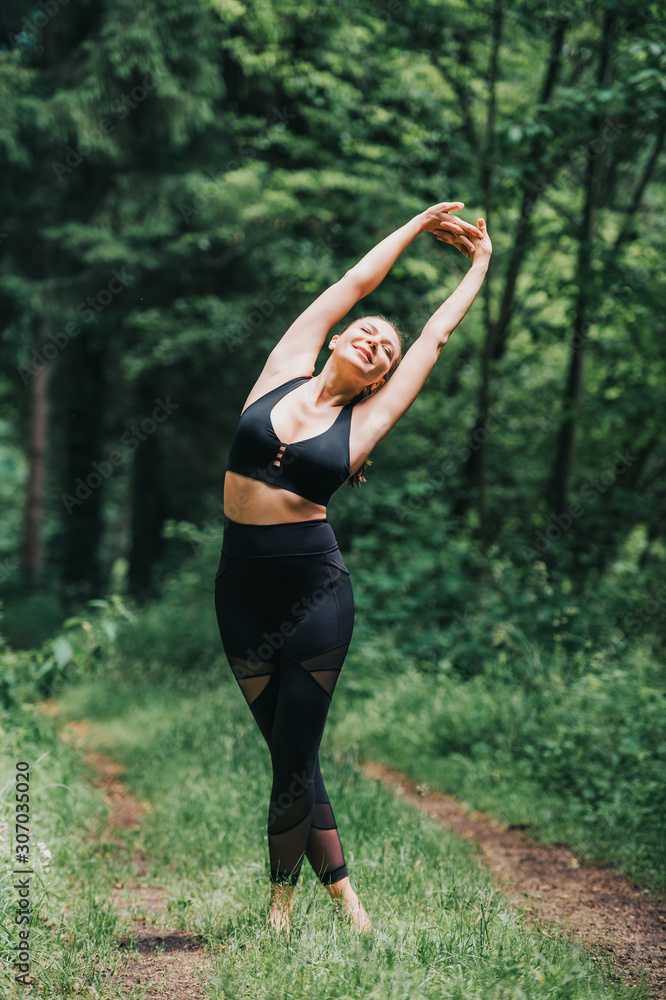 Young fit woman practicing yoga in summer forest, wearing black leggings and top Young fit woman practicing yoga in summer forest, wearing black leggings and top