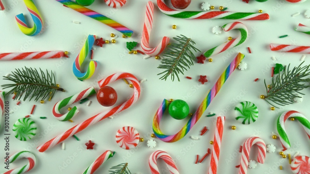 Obraz premium Christmas peppermint candy, red sprinkles and real fir or pine tree branches. Greenery with sugar sweets on white holiday table.