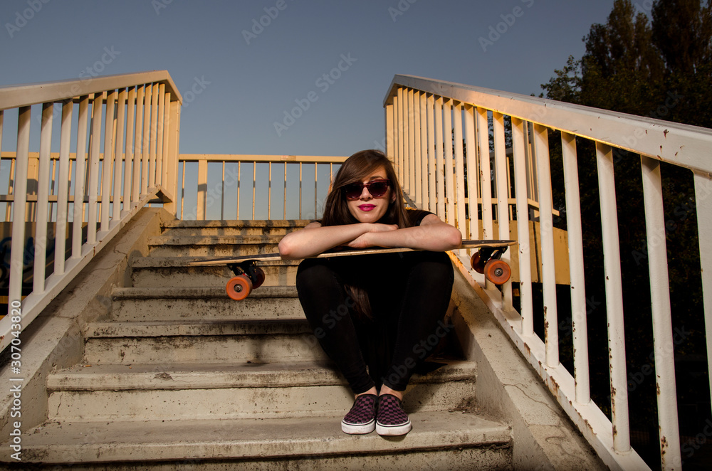 Cute girl posing with her longboard while sitting on stairs 
