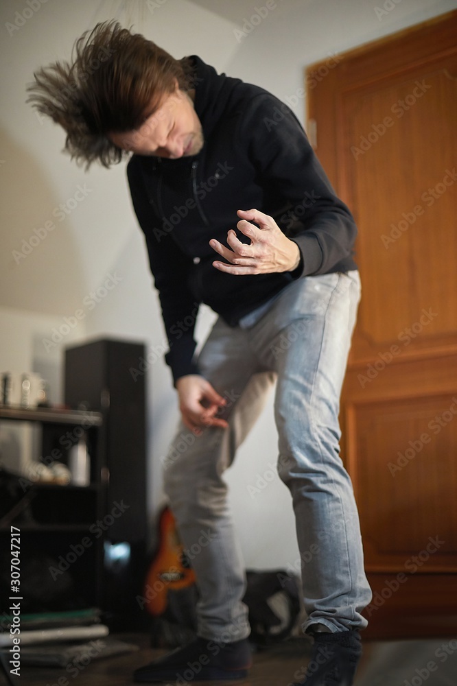 Playing air guitar listening to music in a room, focus on the hand, headbanging head blurred