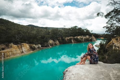 Fototapeta Naklejka Na Ścianę i Meble -  Young girl in dress relaxing on the rock over the Little blue lake in Tasmania with turquoise water