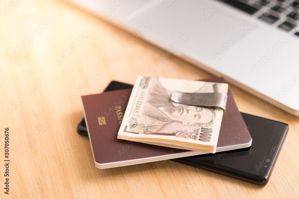 Wads of Japanese cash in money clip pile on top of a passport and smartphone next to computer laptop. Working desk, 10000 Yen, Business trip, Cash-based, Currency exchange rates, Trip expenses, Travel Wads of Japanese cash in money clip pile on top of a passport and smartphone next to computer laptop. Working desk, 10000 Yen, Business trip, Cash-based, Currency exchange rates, Trip expenses, Travel
