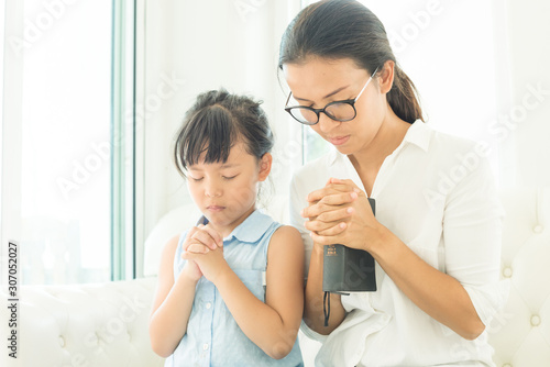 Religious Christian girl praying with her mother indoors