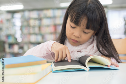 portrait of cute schoolgirl smiling while sitting with stack of books at table in library © nareekarn