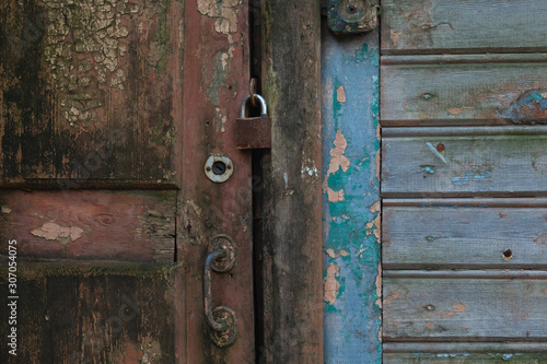 Fragment of an old closed wooden door with cracked brown paint. There is a metal handle and a rusty padlock. Background.