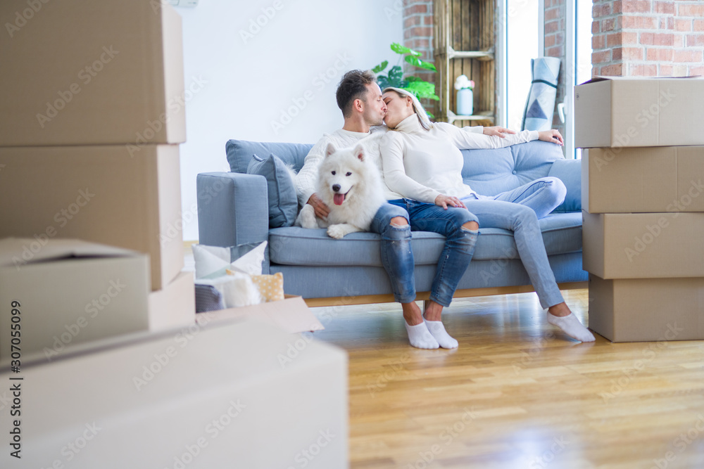 Young beautiful couple with dog kissing sitting on the sofa at new home around cardboard boxes Young beautiful couple with dog kissing sitting on the sofa at new home around cardboard boxes