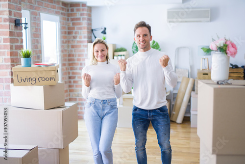 Young beautiful couple standing at new home around cardboard boxes celebrating surprised and amazed for success with arms raised and open eyes. Winner concept. © Krakenimages.com