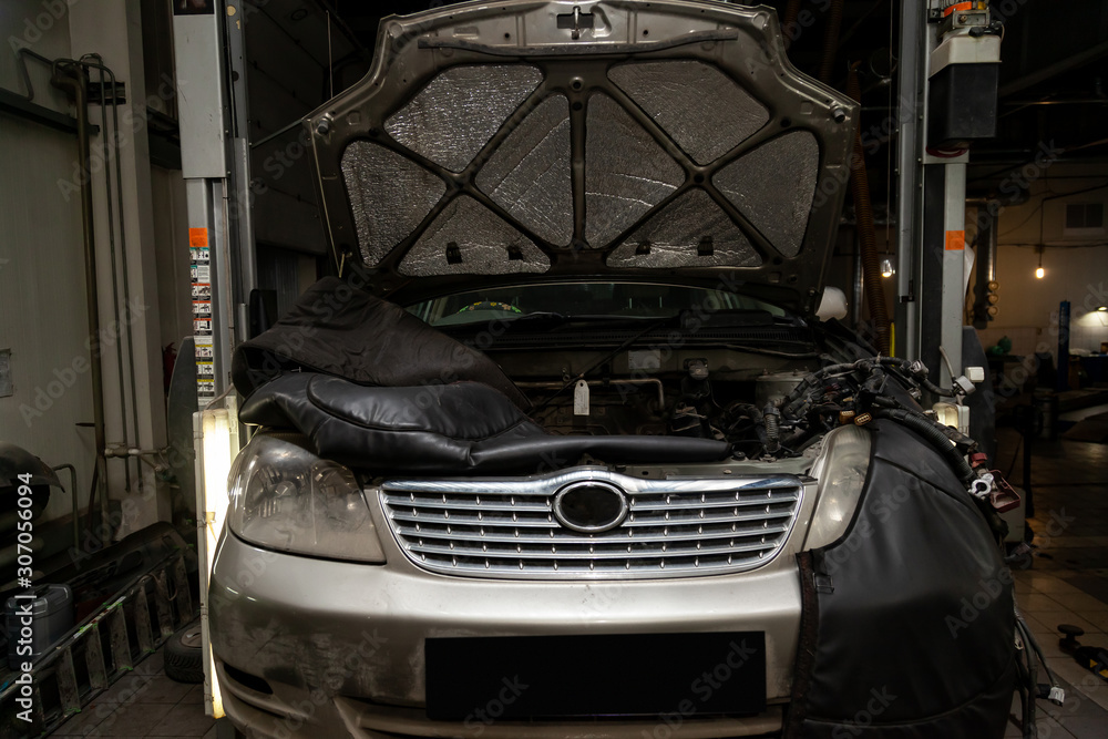 Disassembled gray car in the workshop raised on the lift prepared for repair with opened hood, engine removed, internal equipment, parts visible. Auto service industry. Disassembled gray car in the workshop raised on the lift prepared for repair with opened hood, engine removed, internal equipment, parts visible. Auto service industry.