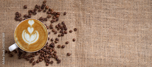 cup of coffee latte and coffee beans on jute panoramic with space for text