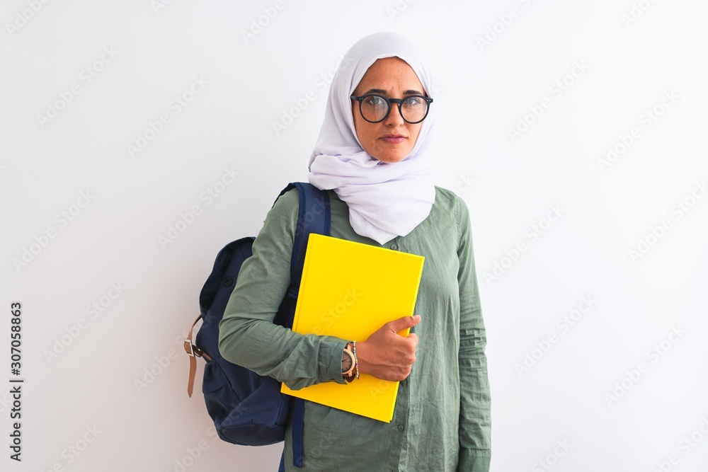 Young Arab student woman wearing hijab and backpack holding a book over isolated background with a confident expression on smart face thinking serious Young Arab student woman wearing hijab and backpack holding a book over isolated background with a confident expression on smart face thinking serious