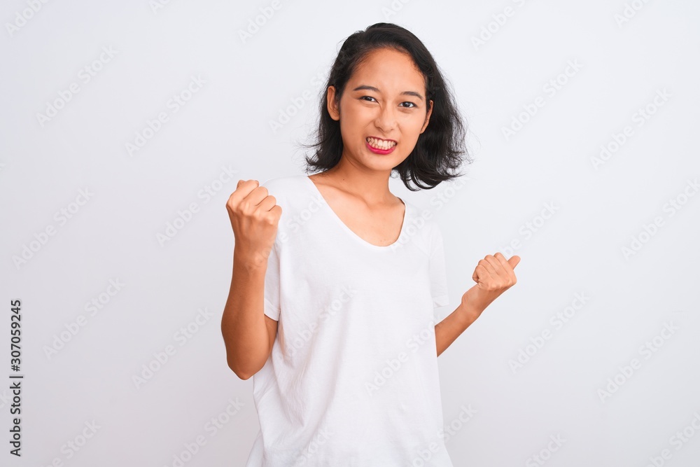 Young chinese woman wearing casual t-shirt standing over isolated white background very happy and excited doing winner gesture with arms raised, smiling and screaming for success. Celebration concept. Young chinese woman wearing casual t-shirt standing over isolated white background very happy and excited doing winner gesture with arms raised, smiling and screaming for success. Celebration concept.