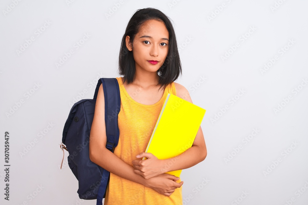 Young chinese student woman wearing backpack holding book over isolated white background with a confident expression on smart face thinking serious Young chinese student woman wearing backpack holding book over isolated white background with a confident expression on smart face thinking serious