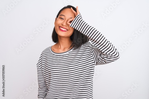 Young chinese woman wearing striped t-shirt standing over isolated white background doing ok gesture with hand smiling, eye looking through fingers with happy face. © Krakenimages.com