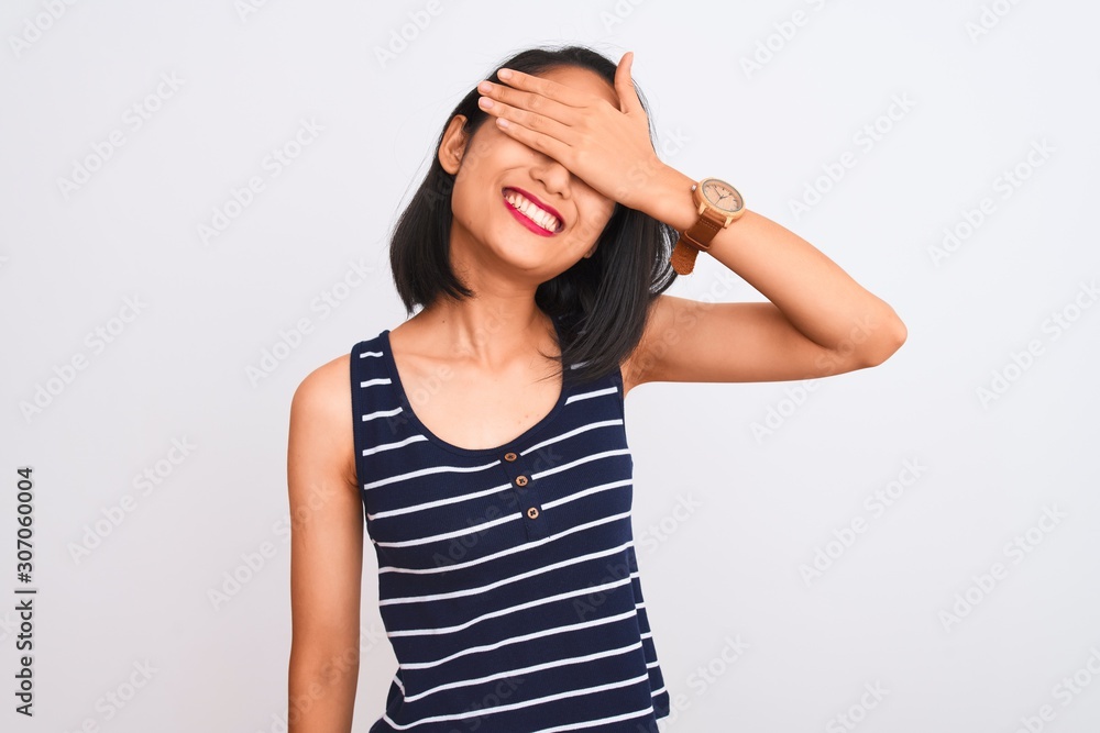 Young chinese woman wearing striped t-shirt standing over isolated white background smiling and laughing with hand on face covering eyes for surprise. Blind concept. Young chinese woman wearing striped t-shirt standing over isolated white background smiling and laughing with hand on face covering eyes for surprise. Blind concept.
