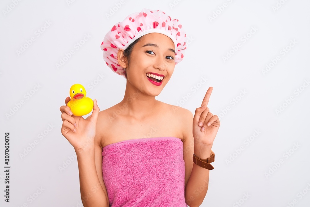 Chinese woman wearing shower towel and cap holding duck toy over isolated white background surprised with an idea or question pointing finger with happy face, number one Chinese woman wearing shower towel and cap holding duck toy over isolated white background surprised with an idea or question pointing finger with happy face, number one