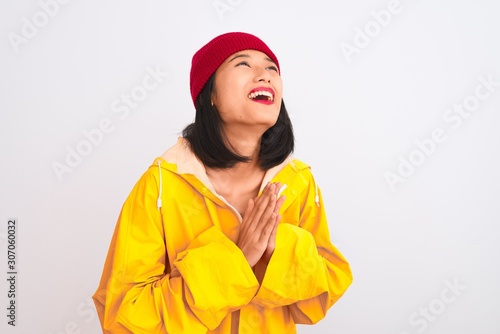 Young beautiful chinese woman wearing raincoat and wool cap over isolated white background begging and praying with hands together with hope expression on face very emotional and worried.  © Krakenimages.com