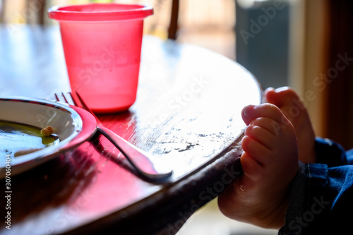 Young Caucasian child with feet resting on the edge of a kitchen table with a fork, cup, and plate visible photo