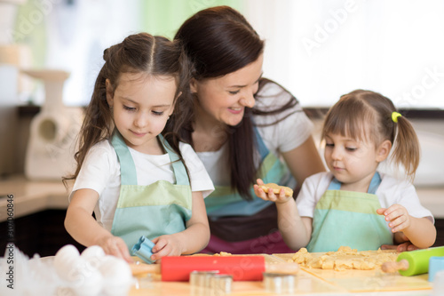 Happy family mother and kids preparing bakery together. Mom and children having fun cooking cookies in the kitchen. Homemade food and little helpers.