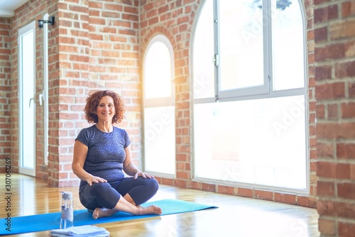 Middle age beautiful sportswoman wearing sportswear sitting on mat practicing yoga at home with a happy and cool smile on face. Lucky person.