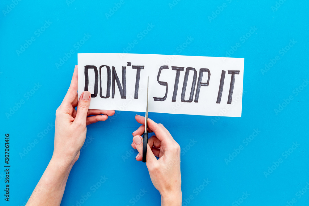 Encouragement and motivation. Hands cutting text Don't stop it with scissors on blue desk Encouragement and motivation. Hands cutting text Don't stop it with scissors on blue desk