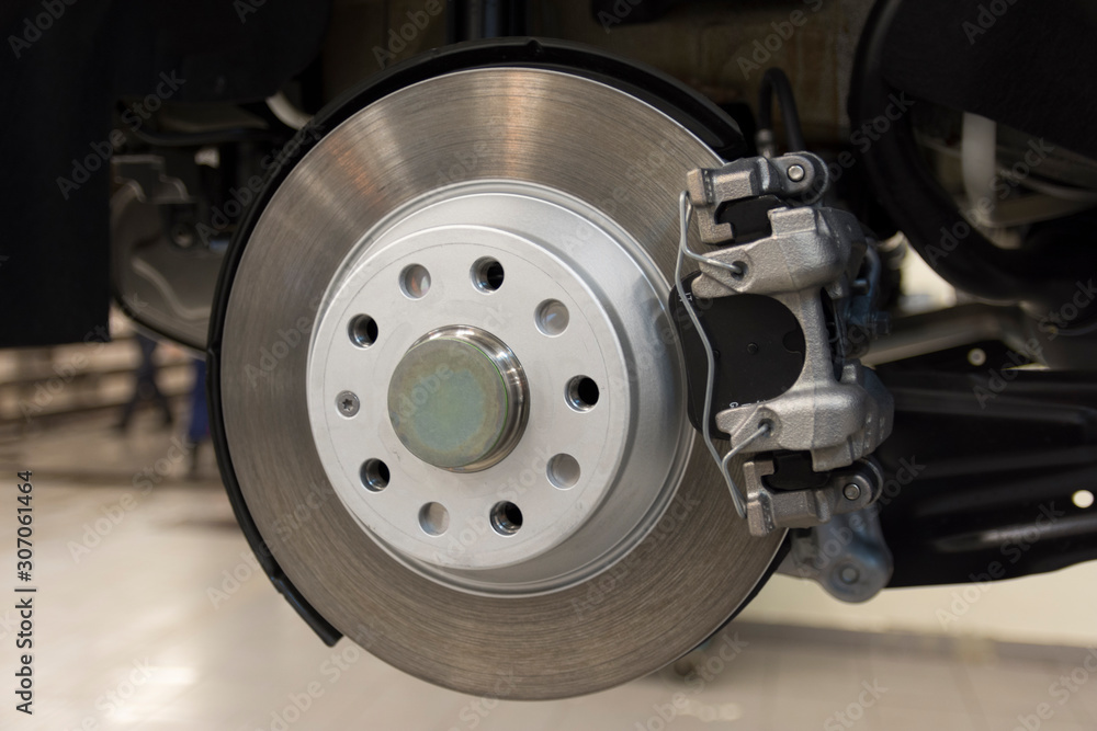 The brake mechanism of a modern car. Rear brake disc of a car with caliper, pads closeup. Technical photography. The brake mechanism of a modern car. Rear brake disc of a car with caliper, pads closeup. Technical photography.