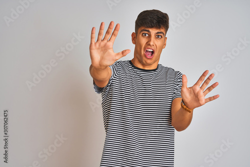 Fotografía Young indian man wearing navy striped t-shirt standing over isolated white background afraid and terrified with fear expression stop gesture with hands, shouting in shock