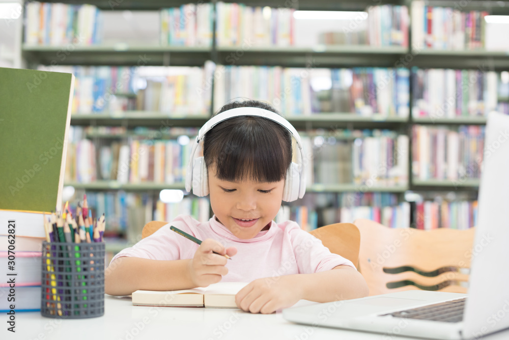Happy smiling girl. Writing a book. And using headphones to listen to music. The computer is on the table. Happy smiling girl. Writing a book. And using headphones to listen to music. The computer is on the table.