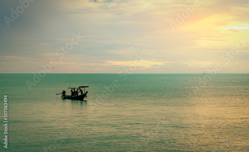 Beautiful tropical sea in the morning with golden sunrise sky. Fisherman in long tail boat with folk fishing culture. Peaceful and tranquil scene. Calm sea in the morning. Seascape with skyline. © Artinun