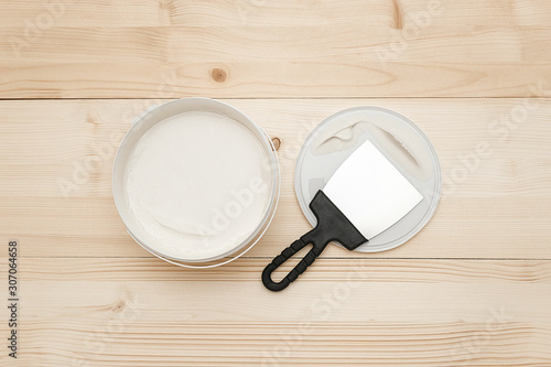 Spatula and a bucket of white putty on wooden boards. Top view Copy space.