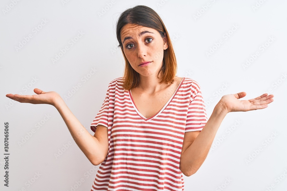 Beautiful redhead woman wearing casual striped red t-shirt over isolated background clueless and confused expression with arms and hands raised. Doubt concept. Beautiful redhead woman wearing casual striped red t-shirt over isolated background clueless and confused expression with arms and hands raised. Doubt concept.