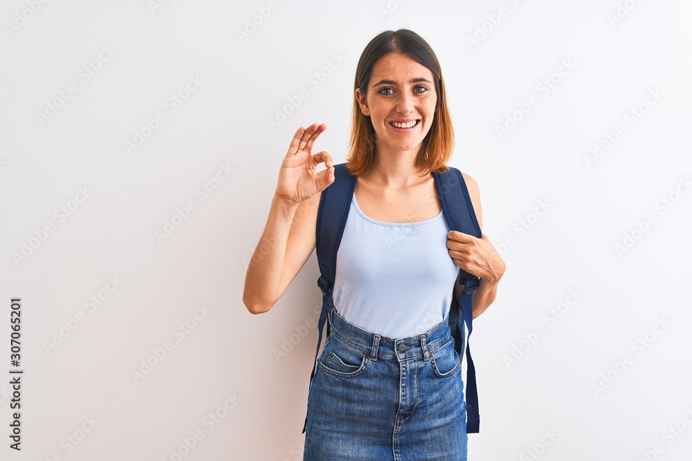 Beautiful redhead student woman wearing a backpack over isolated background doing ok sign with fingers, excellent symbol Beautiful redhead student woman wearing a backpack over isolated background doing ok sign with fingers, excellent symbol