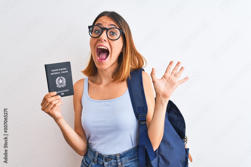 Beautiful redhead student woman wearing backpack and holding passport of italy very happy and excited, winner expression celebrating victory screaming with big smile and raised hands