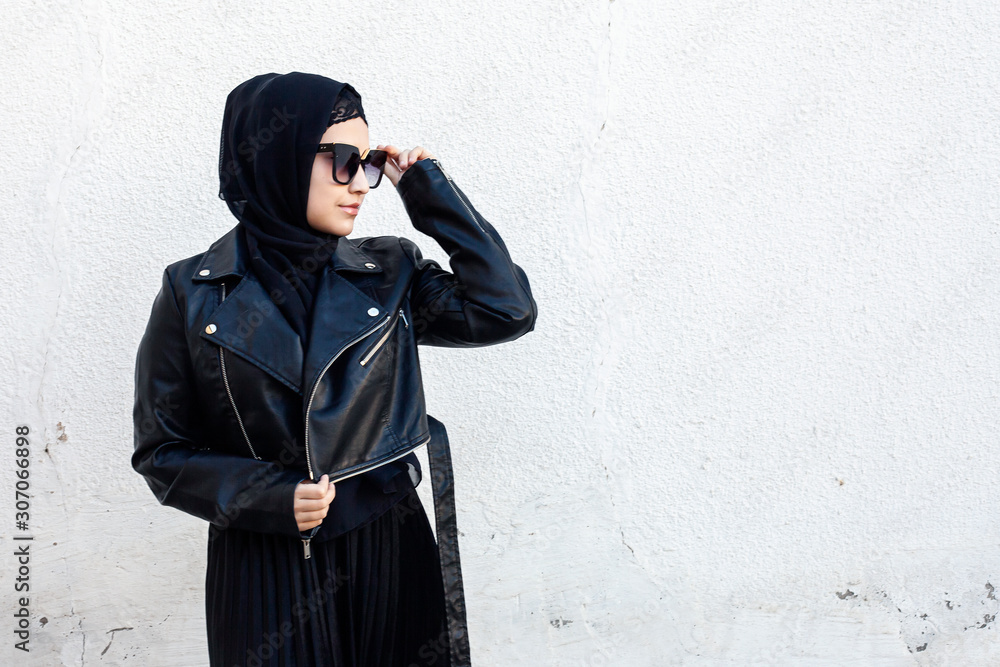Naklejka premium Portrait of beautiful middle-eastern girl in traditional Islamic clothing - hijab. Modern and young Iranian woman in sunglasses and a leather jacket