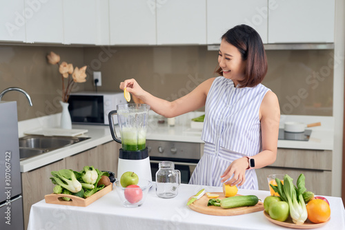 Young Asian woman using blender to make green smoothie in kitchen.