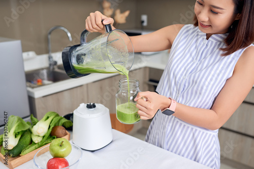 Young Asia woman pouring green smoothie into glass in the modern kitchen