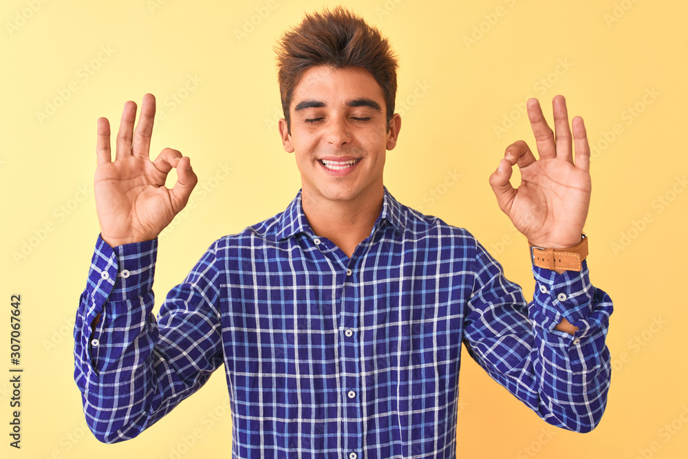 Young handsome man wearing casual shirt standing over isolated yellow background relax and smiling with eyes closed doing meditation gesture with fingers. Yoga concept. Young handsome man wearing casual shirt standing over isolated yellow background relax and smiling with eyes closed doing meditation gesture with fingers. Yoga concept.