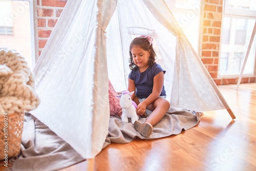 Beautiful toddler girl sitting on the floor playing with unicorn inside tipi at kindergarten
