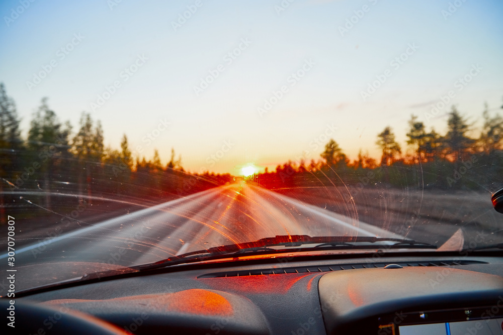 Red sunset view with shining sun from the car front window. Driving car during sunset concept. View on nature landscape and a road from car cabin Red sunset view with shining sun from the car front window. Driving car during sunset concept. View on nature landscape and a road from car cabin