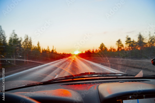 Red sunset view with shining sun from the car front window. Driving car during sunset concept. View on nature landscape and a road from car cabin