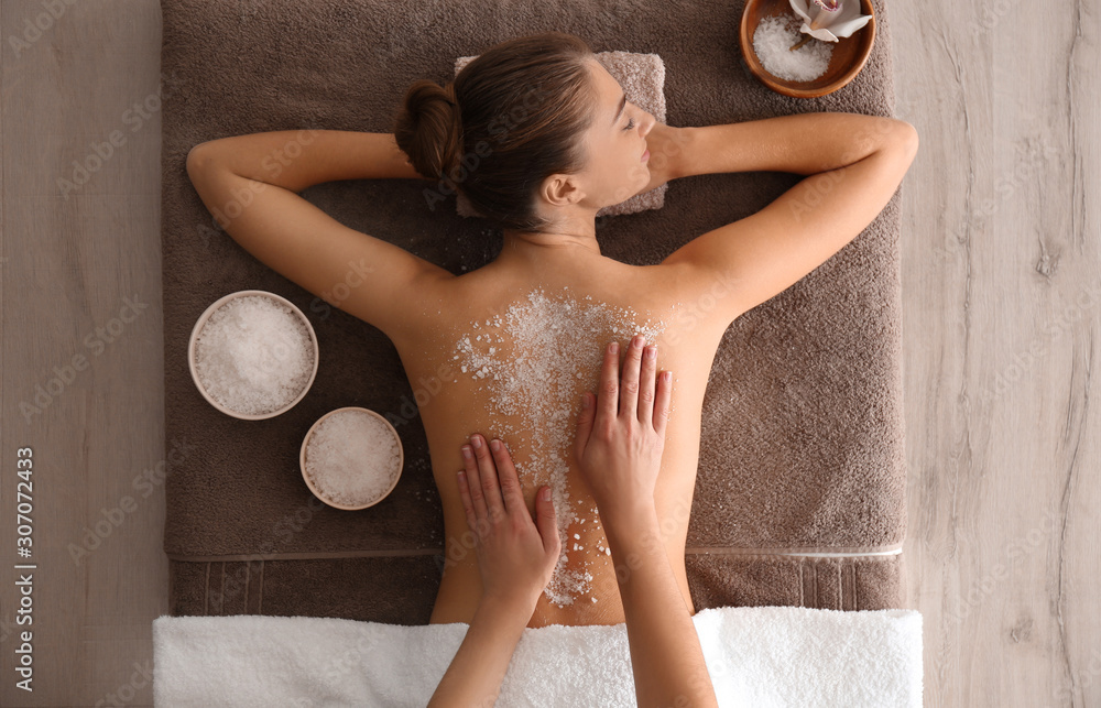 Young woman having body scrubbing procedure with sea salt in spa salon, top view - obrazy, fototapety, plakaty 