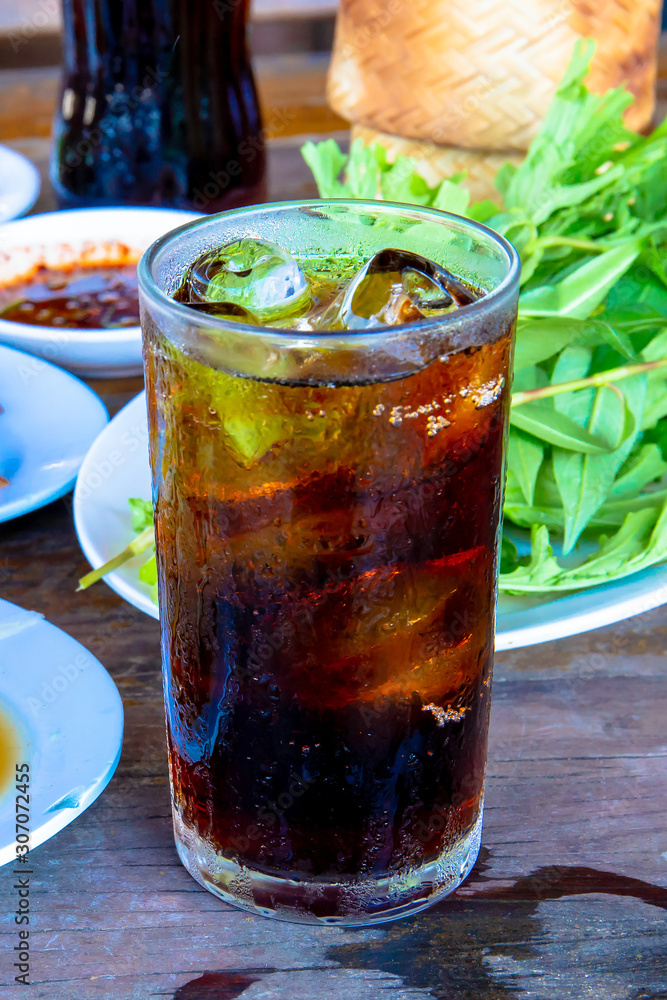 Pop water or cola in glass with ice cubes with food in the background. Pop water or cola in glass with ice cubes with food in the background.