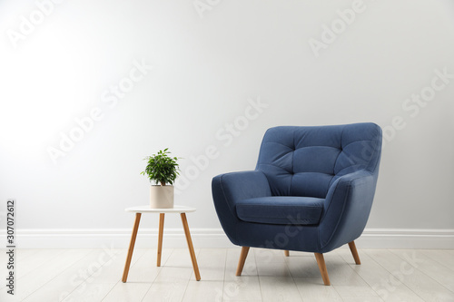 Stylish armchair and table with houseplant near white wall. Interior design © New Africa