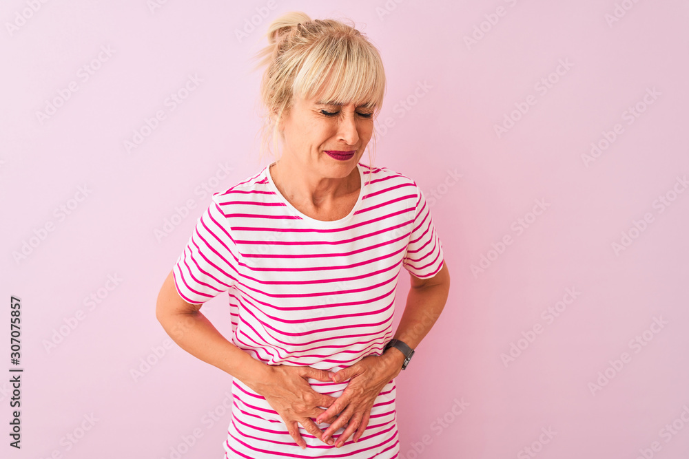 Middle age woman wearing striped t-shirt standing over isolated pink background with hand on stomach because indigestion, painful illness feeling unwell. Ache concept. Middle age woman wearing striped t-shirt standing over isolated pink background with hand on stomach because indigestion, painful illness feeling unwell. Ache concept.