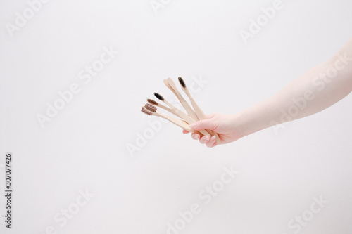 female hand holds bamboo toothbrushes like a bouquet on a light background copy space, zero waste concept, eco-friendly lifestyle