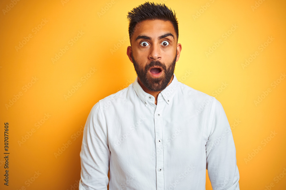 Obraz premium Indian businessman wearing white elegant shirt standing over isolated yellow background afraid and shocked with surprise expression, fear and excited face.