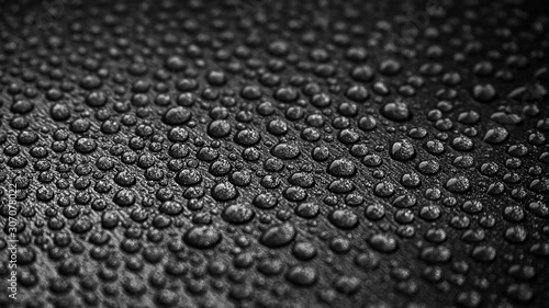 abstract background: many drops of water on a dark surface - non-stick coating in a pan. Center in sharpness, blurred edges. Black and white photo