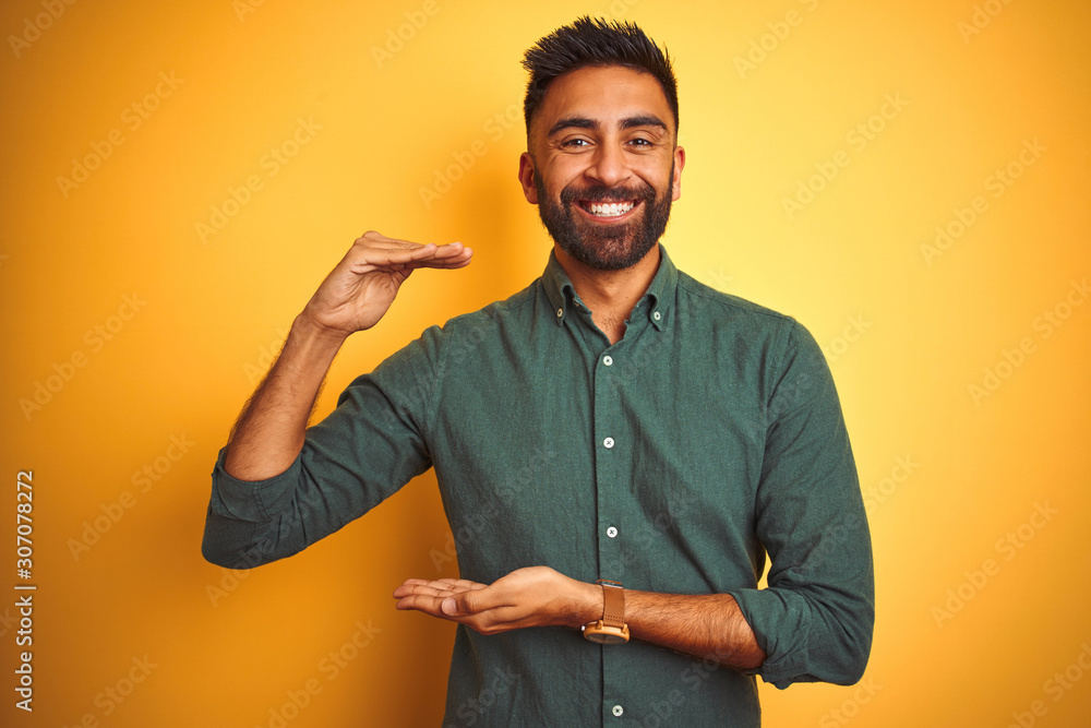 Young indian businessman wearing elegant shirt standing over isolated white background gesturing with hands showing big and large size sign, measure symbol. Smiling looking at the camera. Measuring Young indian businessman wearing elegant shirt standing over isolated white background gesturing with hands showing big and large size sign, measure symbol. Smiling looking at the camera. Measuring