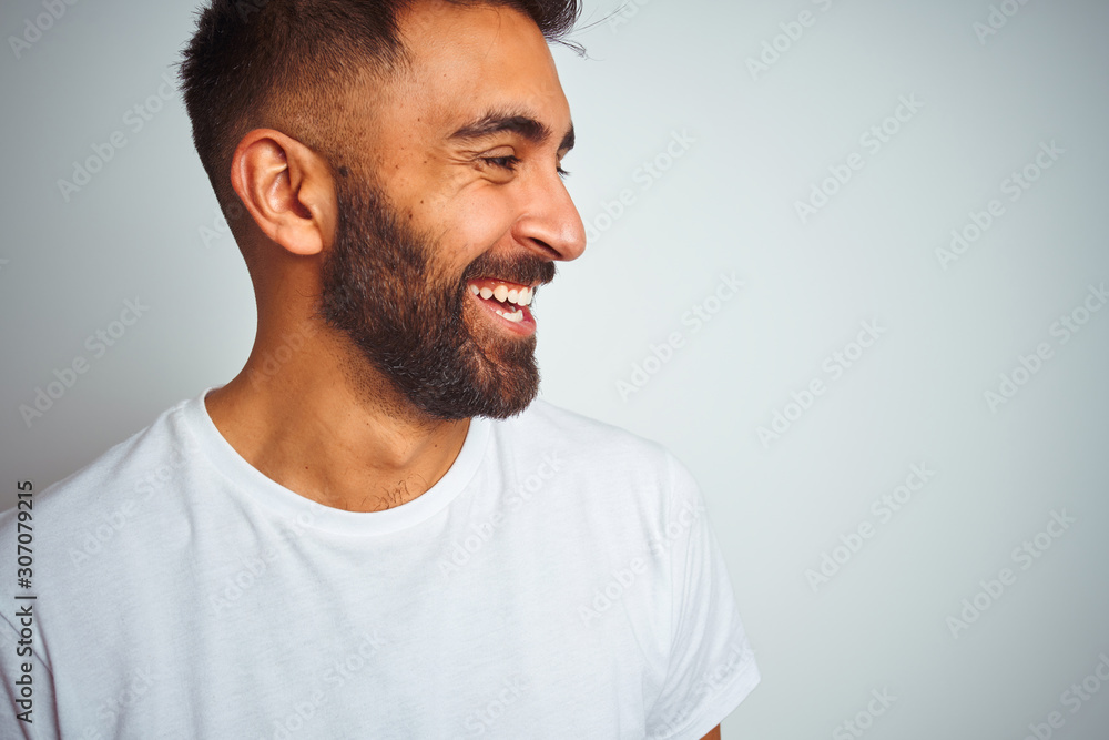 Young indian man wearing t-shirt standing over isolated white background looking away to side with smile on face, natural expression. Laughing confident. Young indian man wearing t-shirt standing over isolated white background looking away to side with smile on face, natural expression. Laughing confident.